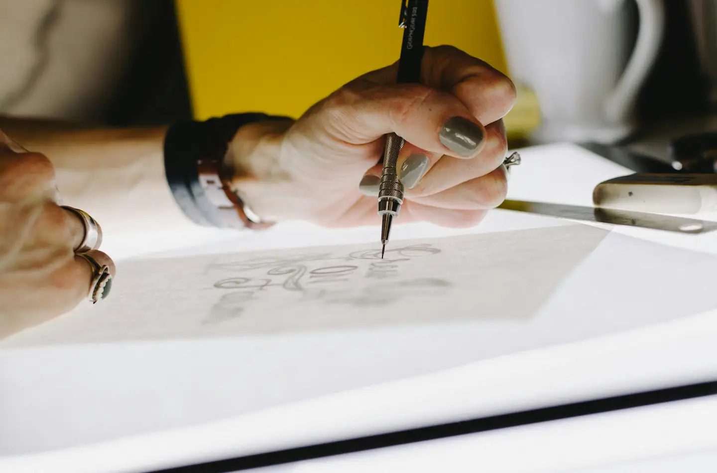 Hand zeichnet mit Feinminenstift Schriftentwürfe auf Transparentpapier