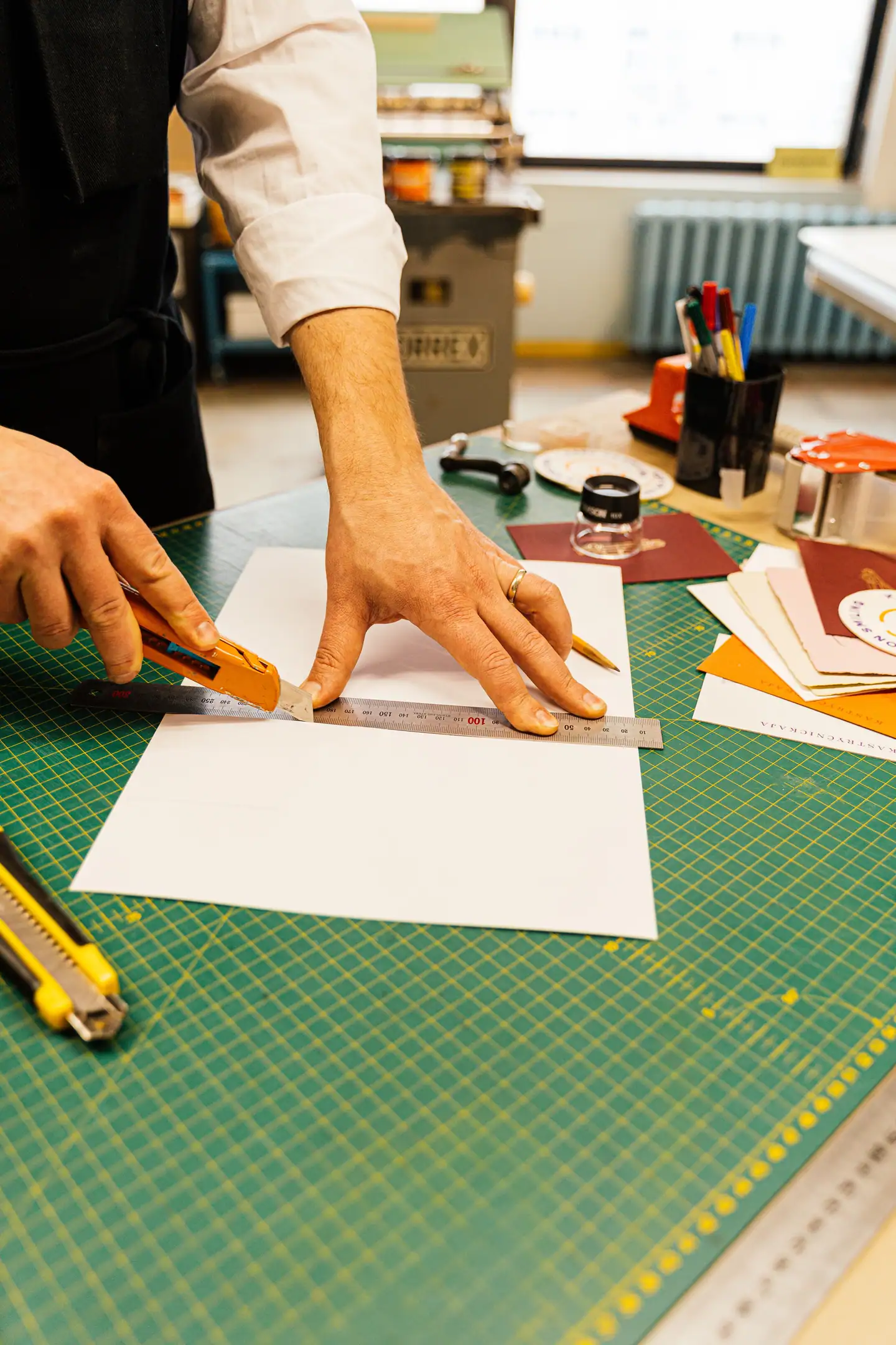 Hände schneiden Papier mit dem Cutter entlang des Stahllineals