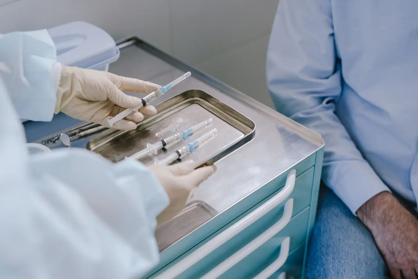 Impfung wird vorbereitet: Spritzen auf der Nierenschale neben dem Patienten