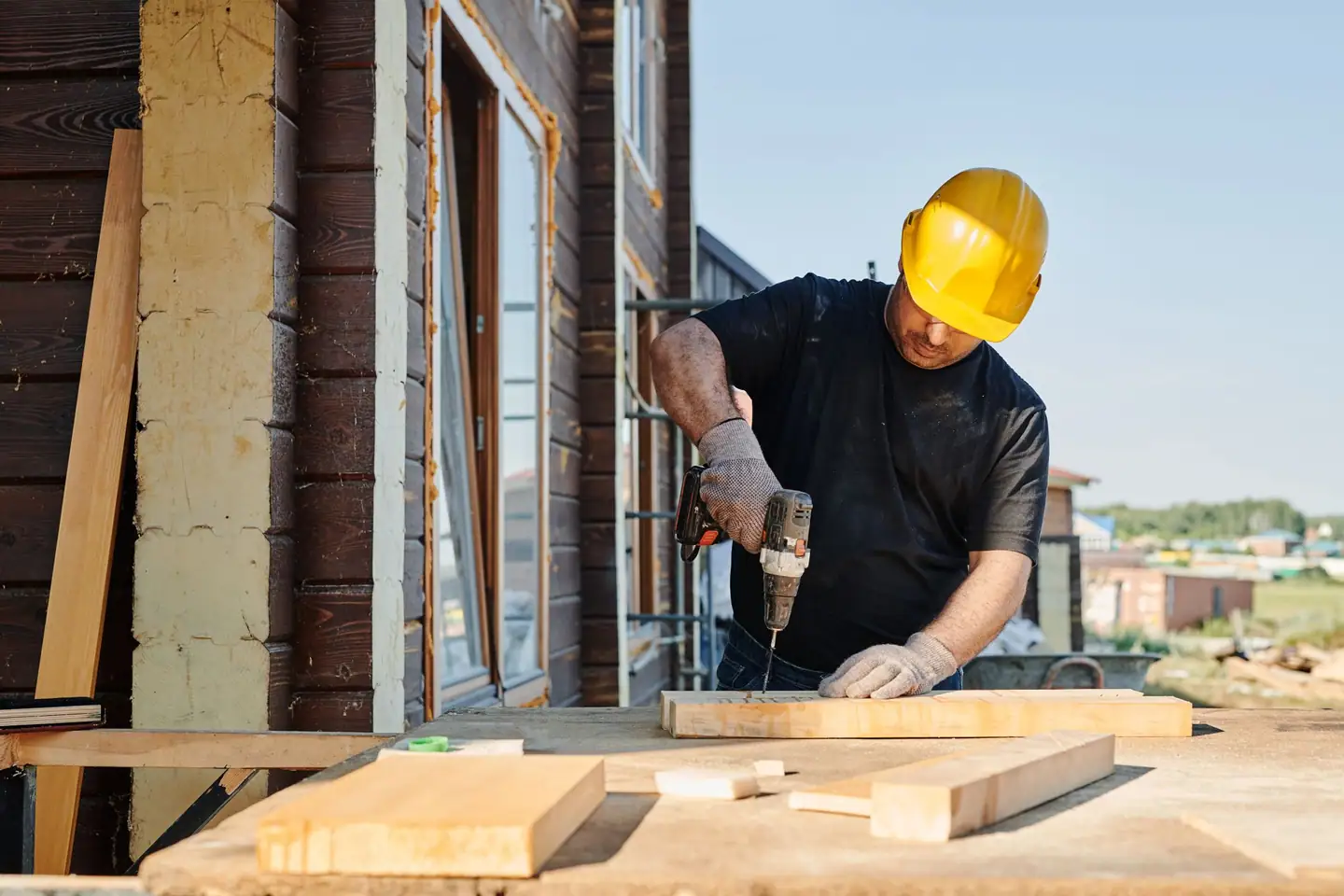 Bauarbeiter mit Helm bohrt auf der Baustelle in ein Kantholz