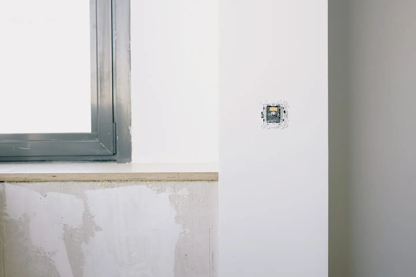Neu gesetzte Steckdose an frisch verputzter Wand neben dem Fenster
