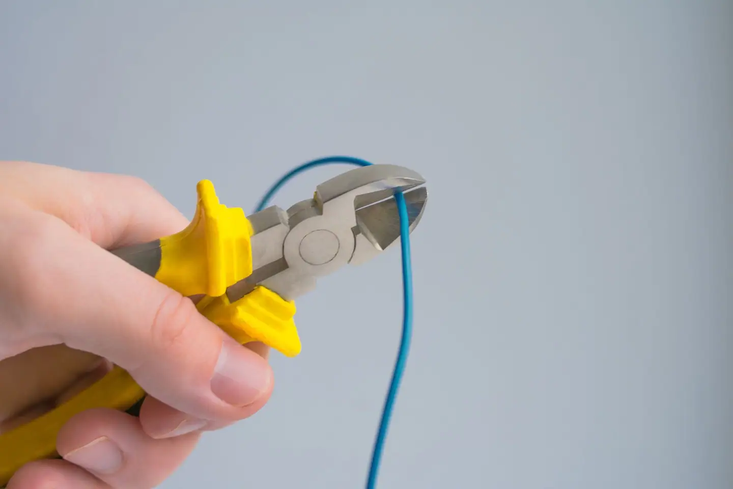 Hand trennt einen blauen Leiter mit dem Seitenschneider