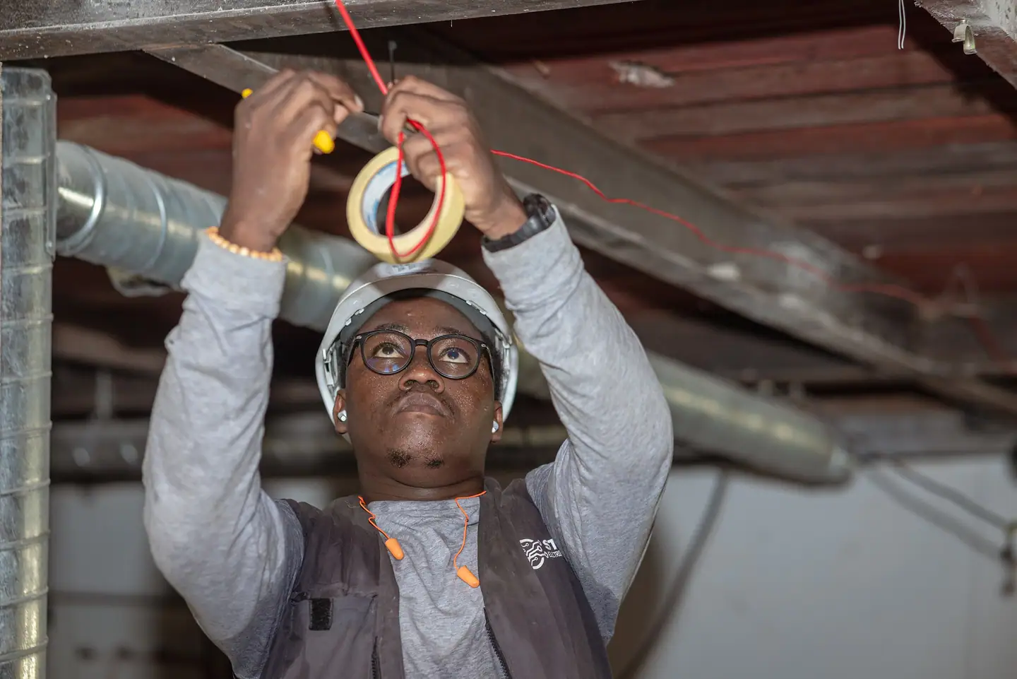 Elektriker mit Helm verlegt Leitungen unter der Decke