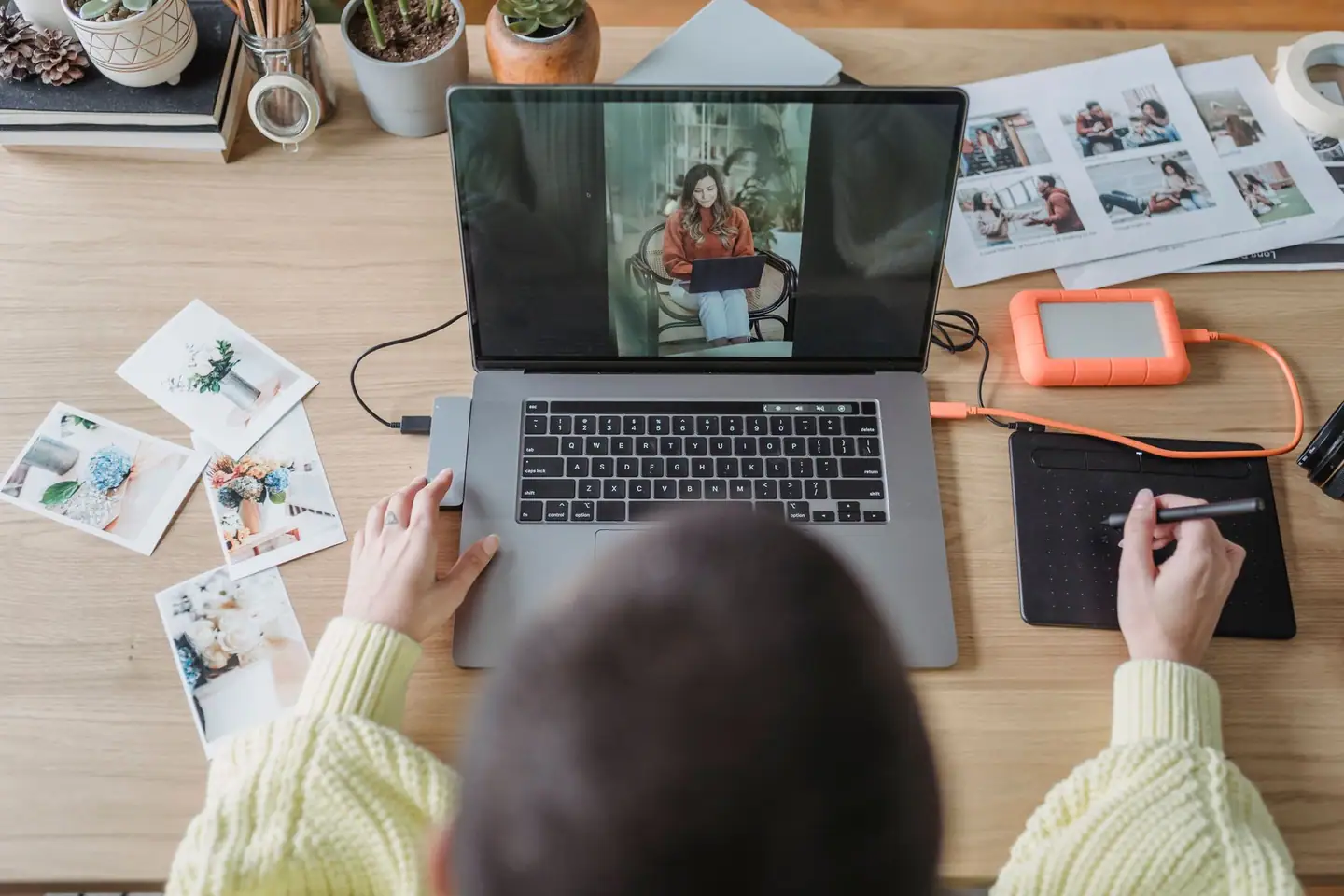 Hände an Laptop und Grafiktablett bei der Bildbearbeitung, Abzüge auf dem Tisch