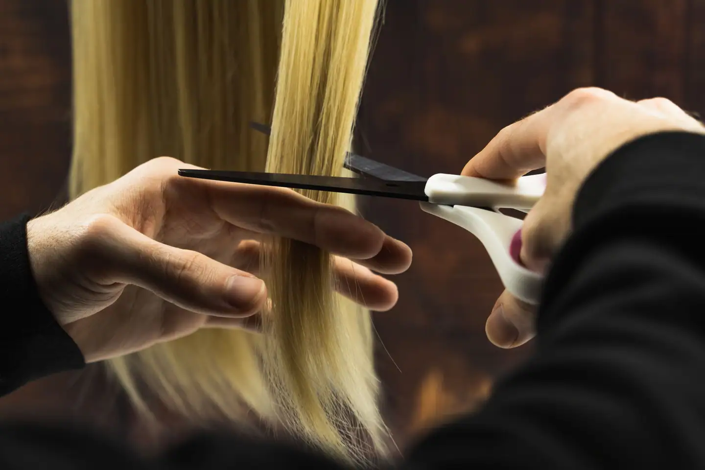 Hände schneiden eine blonde Haarsträhne mit Schere und Kamm