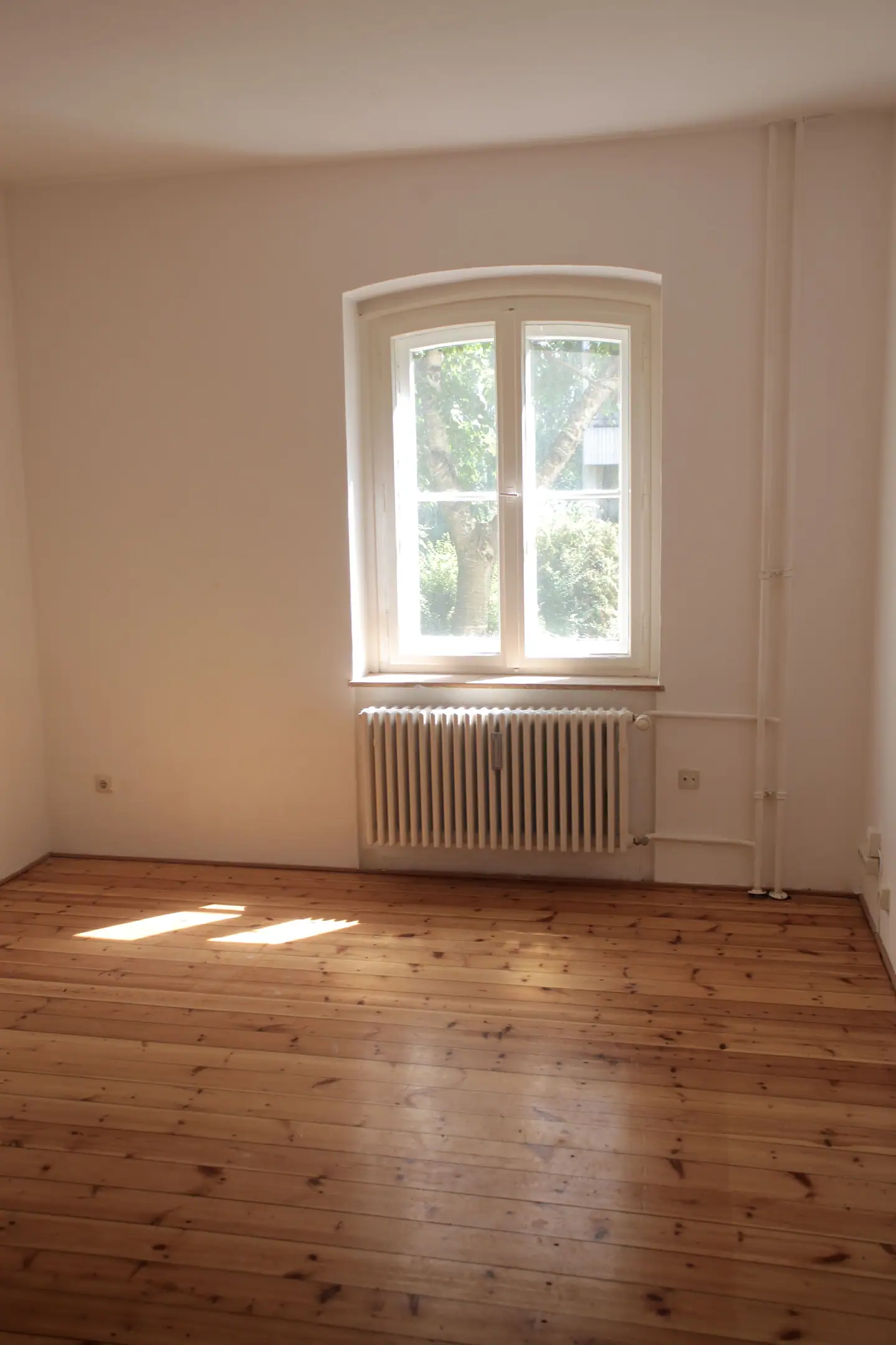 Leeres Zimmer mit Dielenboden, Sprossenfenster und Heizkörper in der Sonne