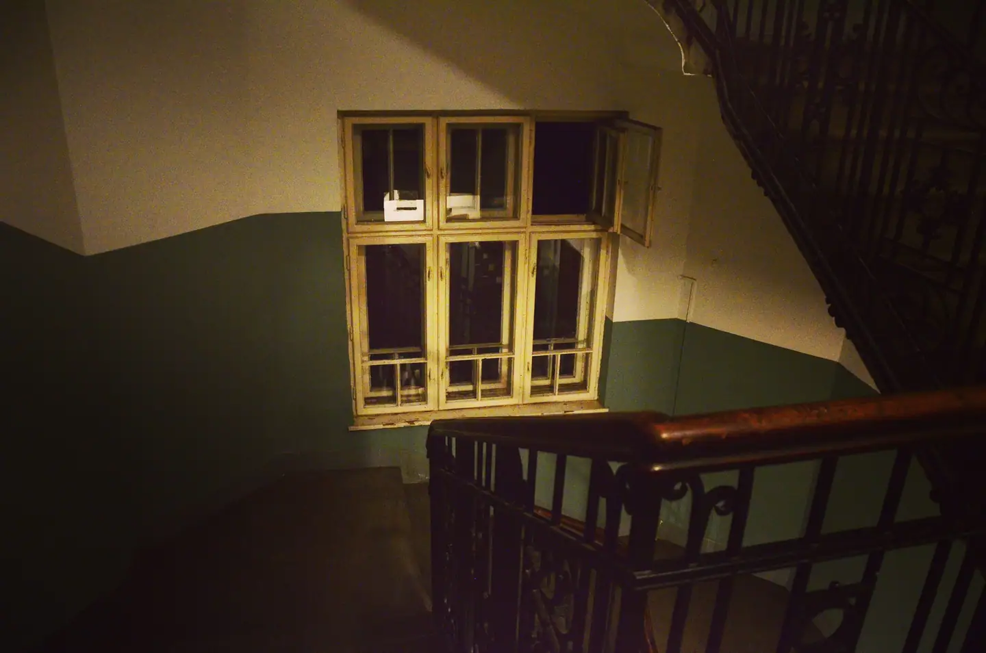 Abendliches Stiegenhaus mit Holzhandlauf, Schmiedeeisengeländer und Kastenfenster