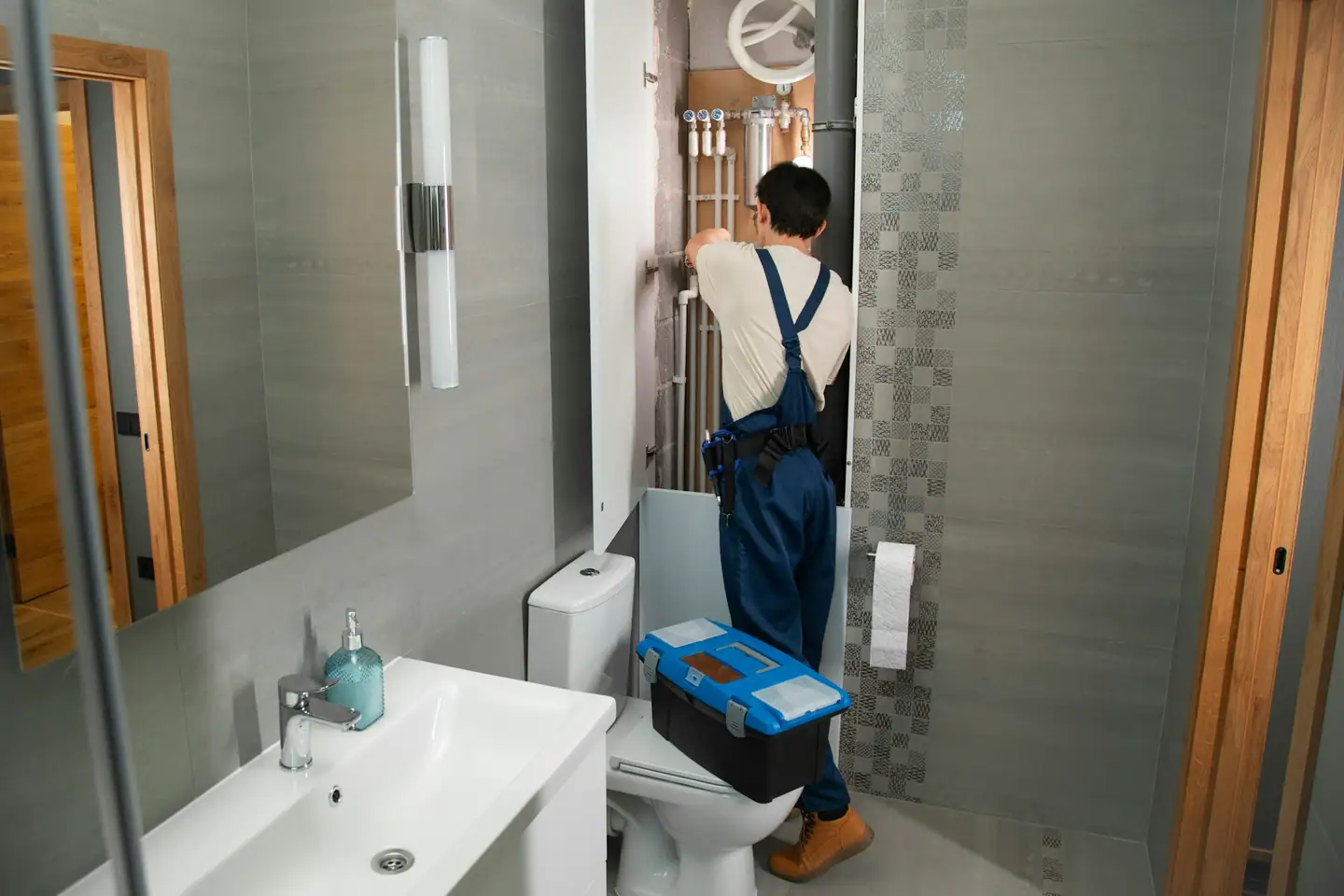 Installateur im Arbeitsoverall an offener Vorwandinstallation im neuen Bad