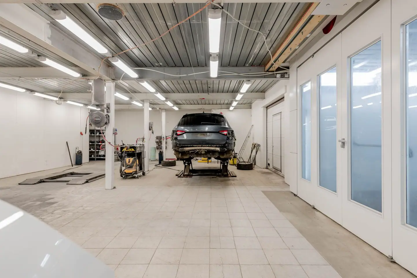 Helle Werkstatthalle mit Fliesenboden, hinten ein Auto auf der Hebebühne