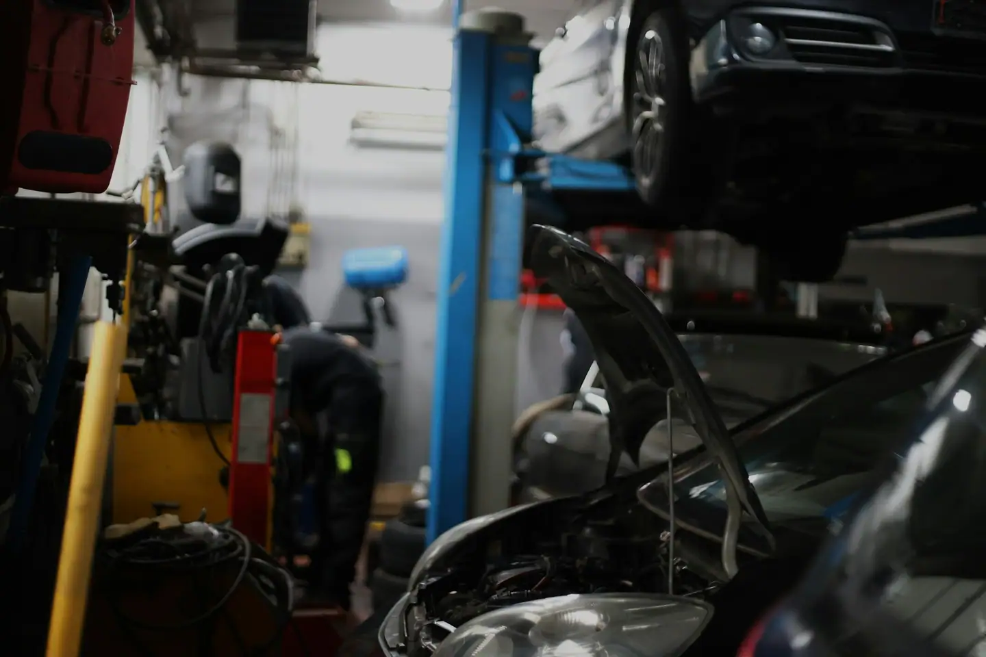 Werkstatt mit Hebebühne, offener Motorhaube und Mechaniker im Hintergrund