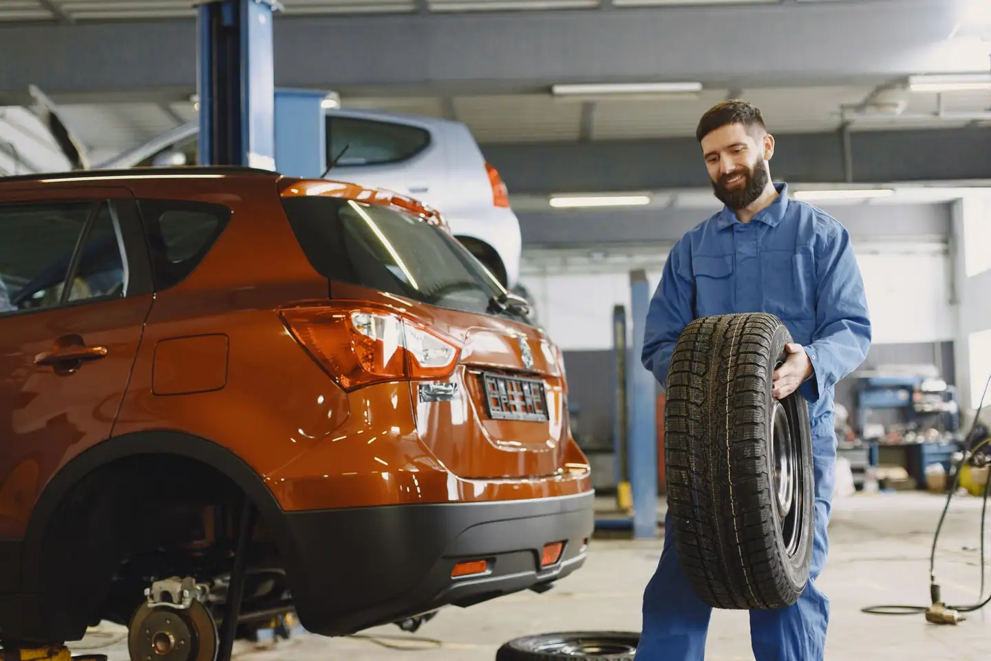 Mechaniker trägt beim Reifenwechsel einen Winterreifen zum Auto
