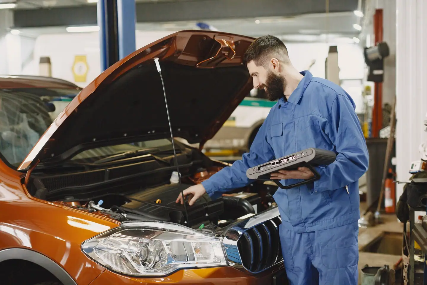 Mechaniker im Overall prüft den Motor mit einem Diagnosegerät in der Hand