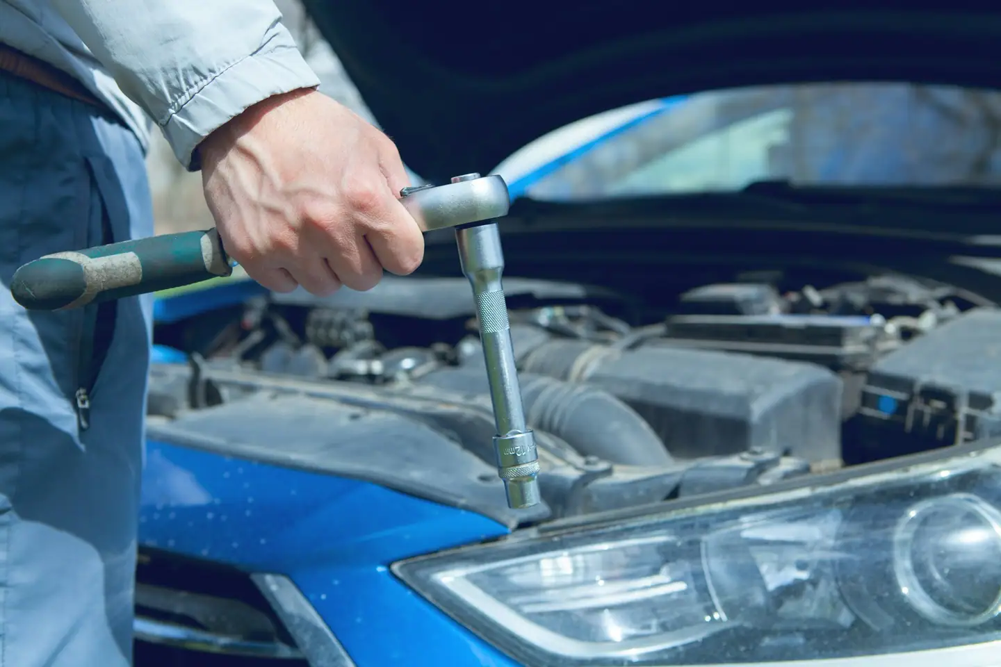 Hand mit Ratsche beim Schrauben im Motorraum