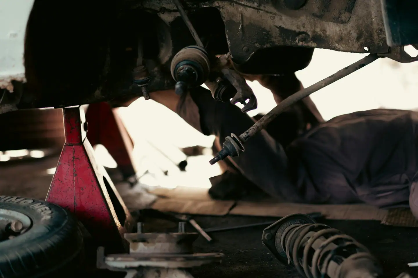 Mechaniker arbeitet unter dem aufgebockten Auto an der Radaufhängung