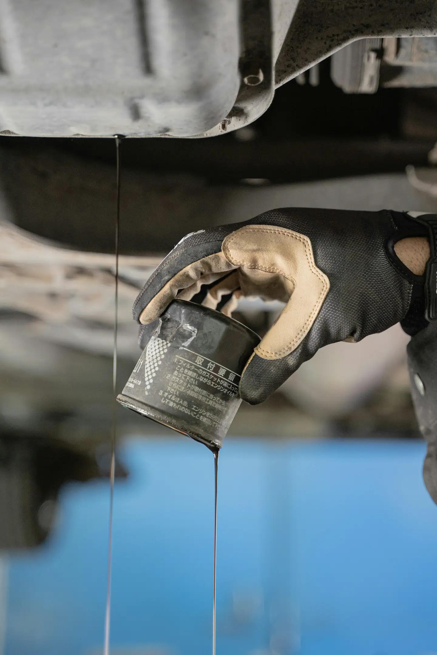 Ölwechsel: Hand im Handschuh hält den alten Ölfilter unter dem Auto