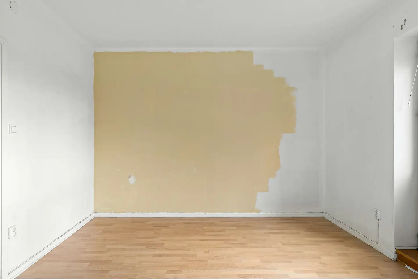 Zimmer mit Laminatboden, eine Wand halb in Sandgelb gestrichen