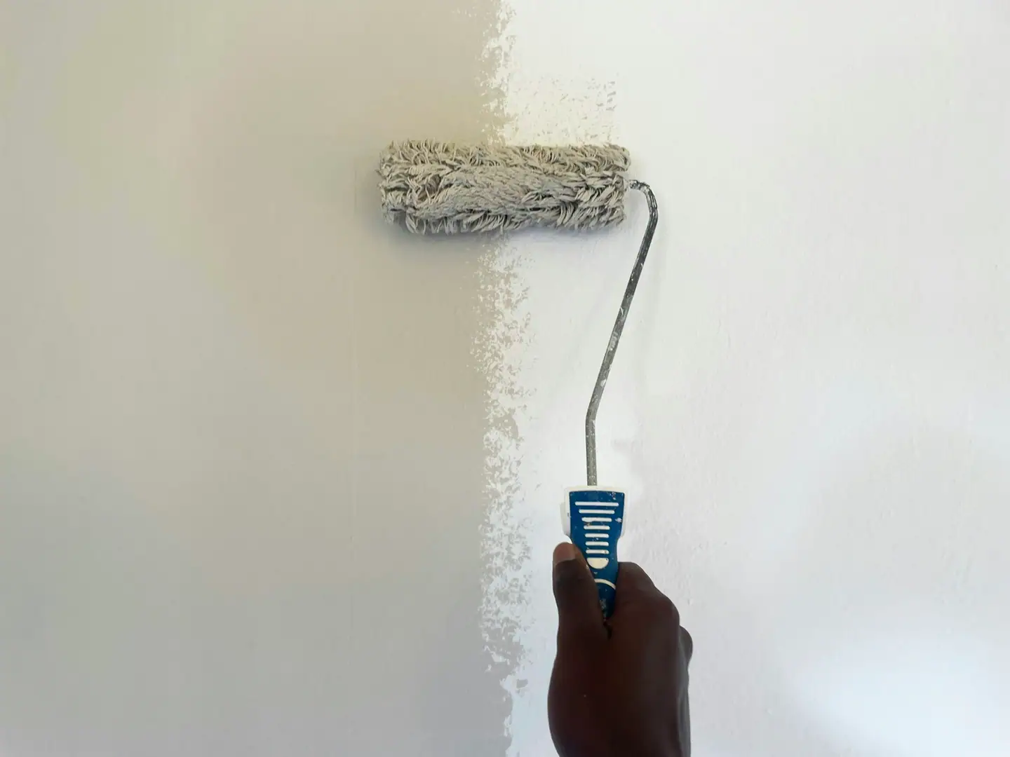 Hand rollt weiße Farbe gleichmäßig auf eine Innenwand