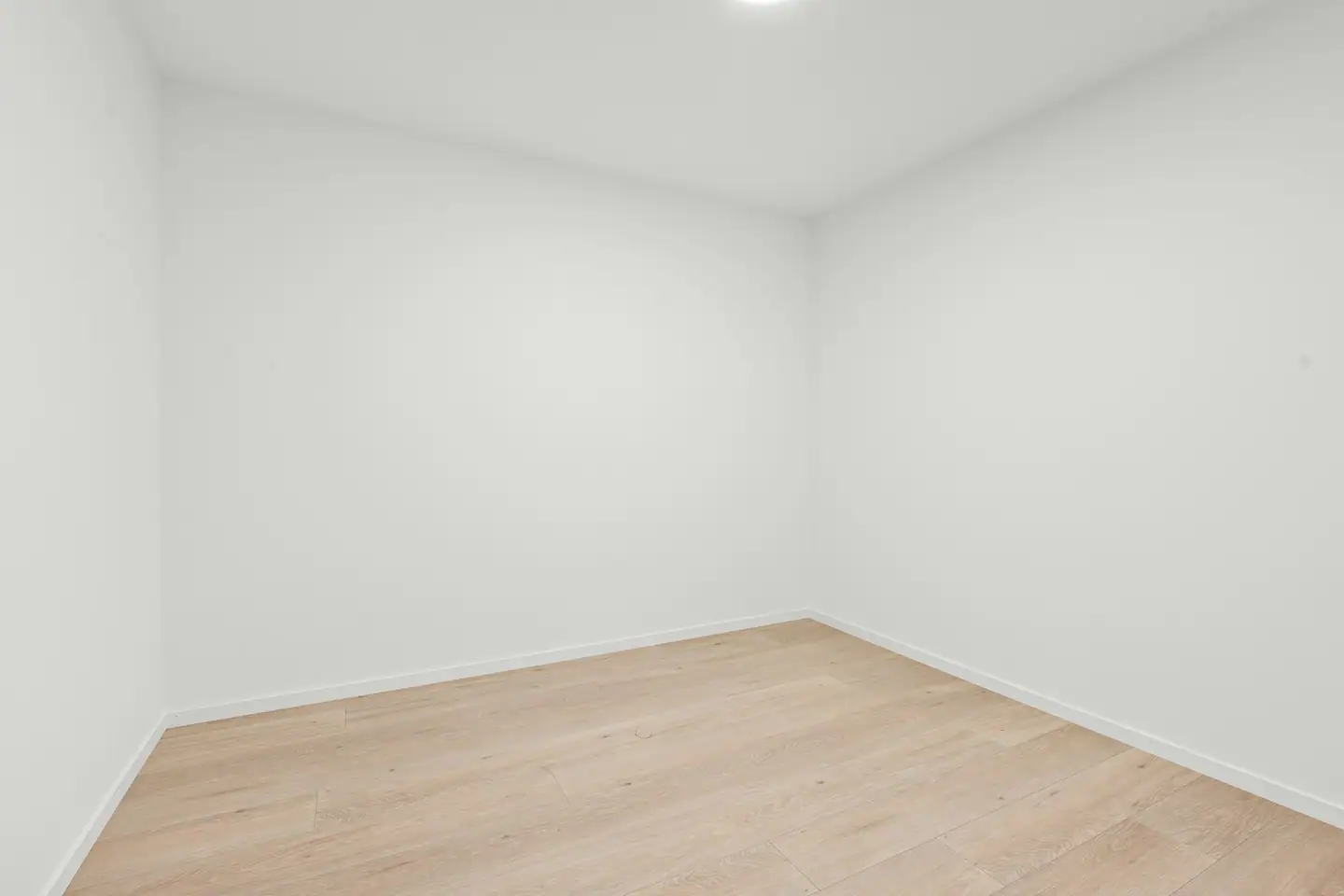 Frisch ausgemaltes, leeres Zimmer mit weißen Wänden und hellem Holzboden