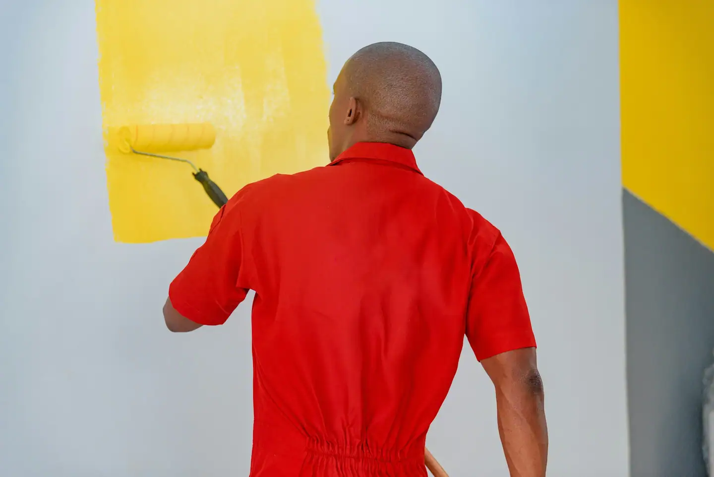 Maler im roten Overall rollt gelbe Farbe auf eine Wand