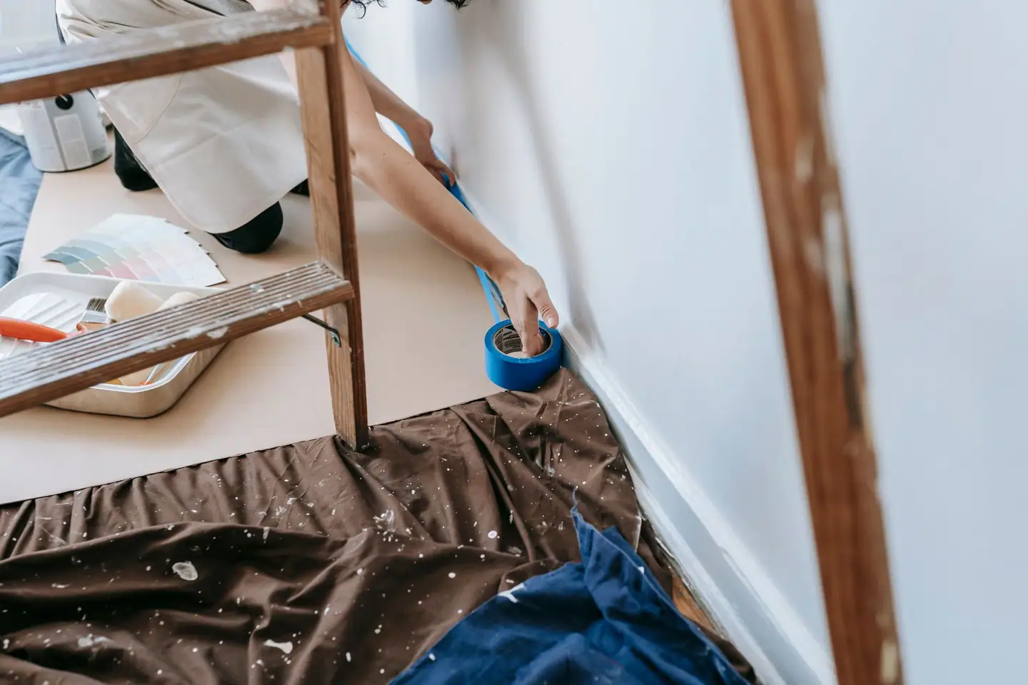 Malerkrepp wird an der Sockelleiste geklebt, Boden mit Folie abgedeckt