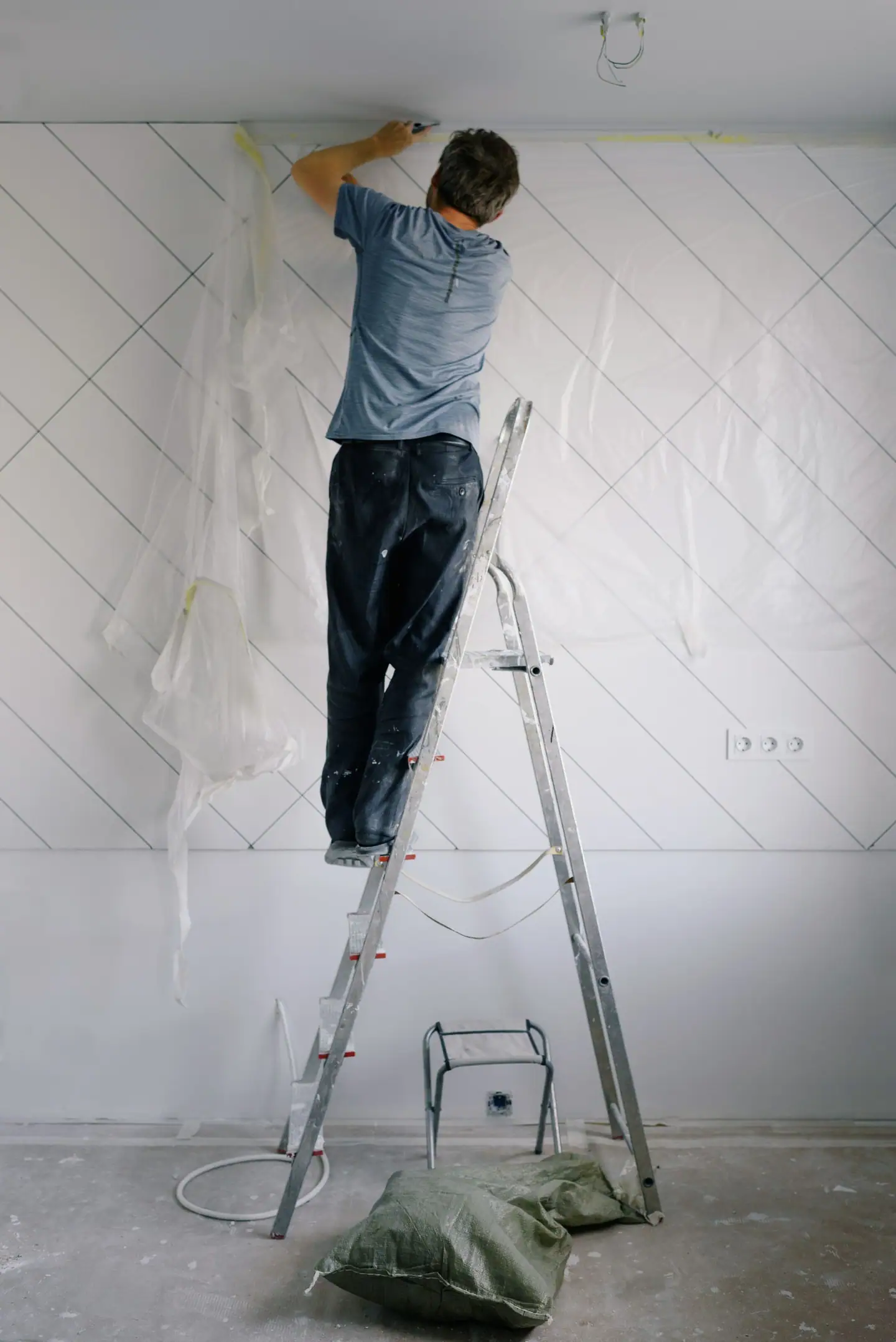 Maler auf der Stehleiter bearbeitet die Wand eines leeren Raums